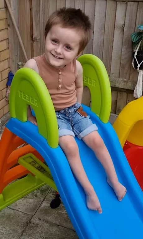 Colby is sitting on top of a children's slide. He is looking at someone off-camera.