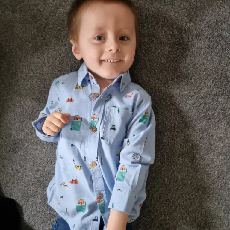 Colby is lying on his back on a carpet. He is wearing a blue shirt.