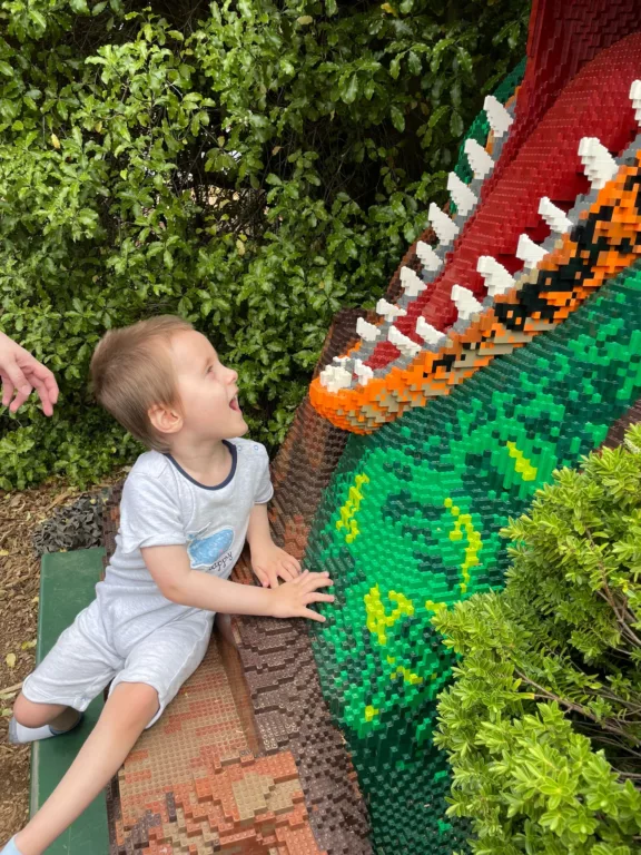 Colby is sitting on the ground in front of a giant dinosaur's mouth.