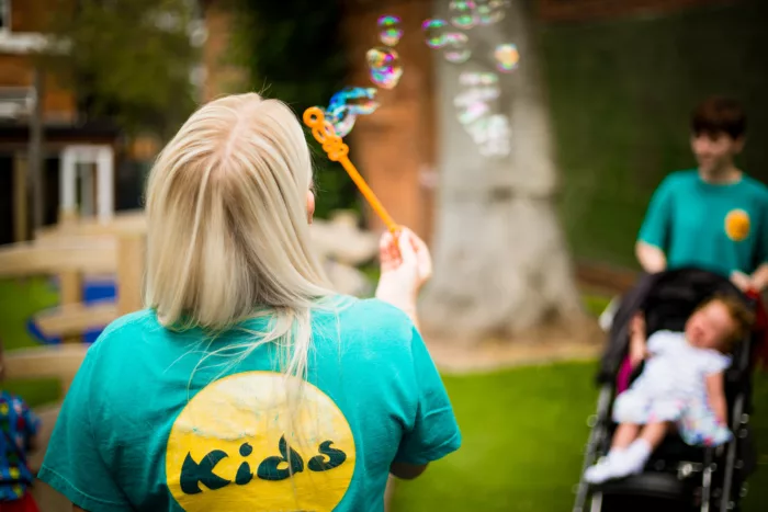 A woman with blonde hair is photographed from behind. She is blowing bubbles.