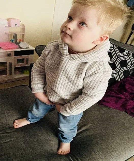 Jenson is photographed from above. He is standing on the sofa with his hands on his hips.