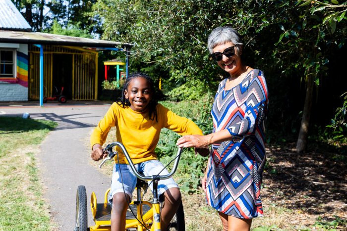A child is sitting on a bike. There is a woman standing on the right, one hand on the bike handle
